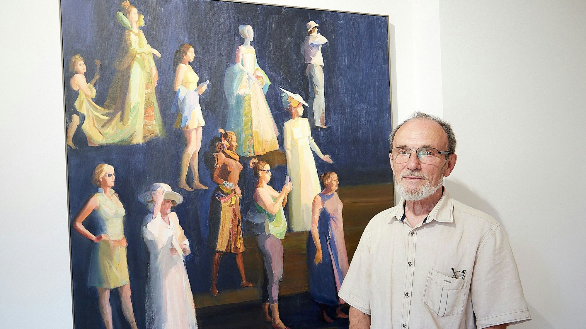 Ein Mann steht vor einem Bild, das Menschen in verschiedenen Bekleidungen zeigt.