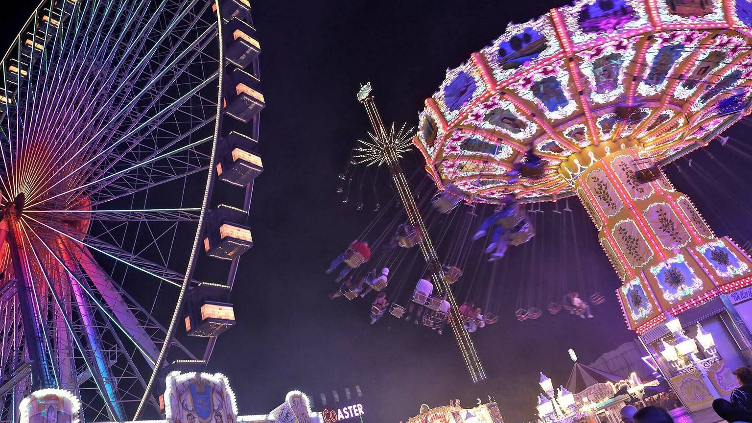 Ein Riesenrad und Kettenkarussell sind hell beleuchtet.