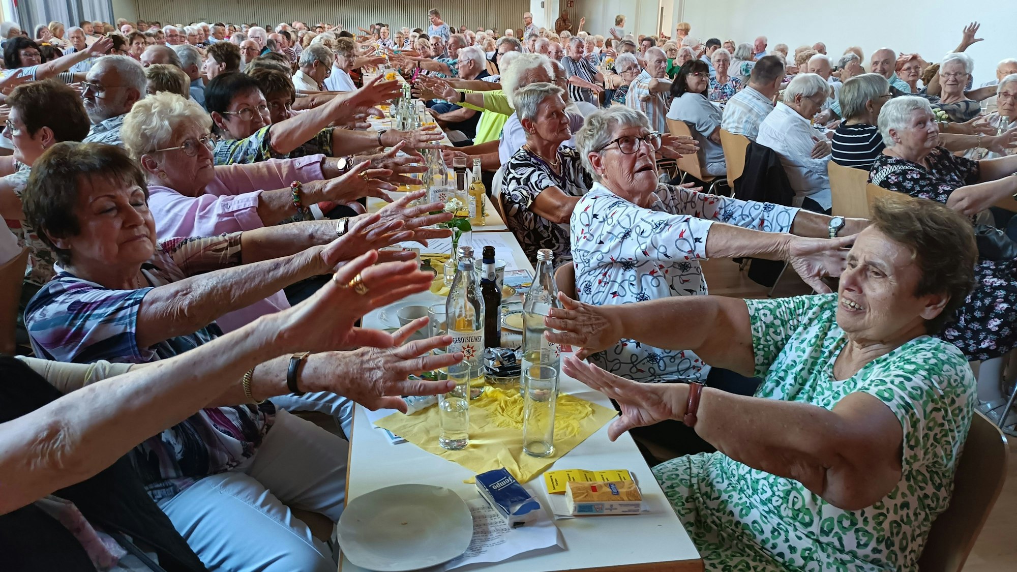 Menschen sitzen an Tischen und strecken die Hände aus.