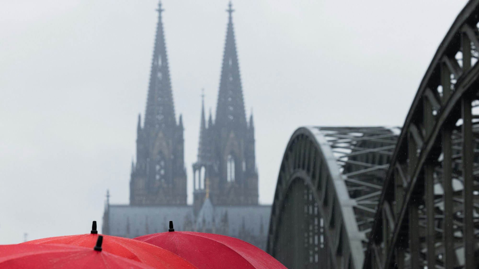 Eine Touristengruppe steht bei Regen mit Regenschirmen auf der Hohenzollernbrücke und schaut auf den Dom.( (Symbolbild)