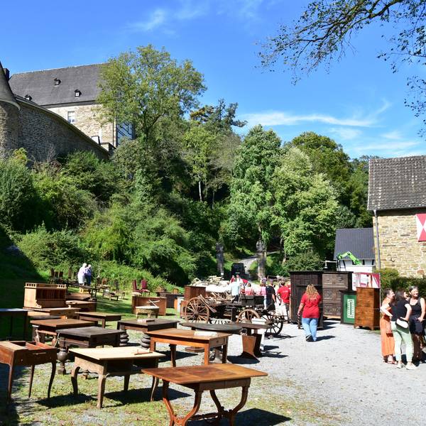 Eine alte Burg, auf einem Schotterplatz im Vordergrund stehen alte Möbel.