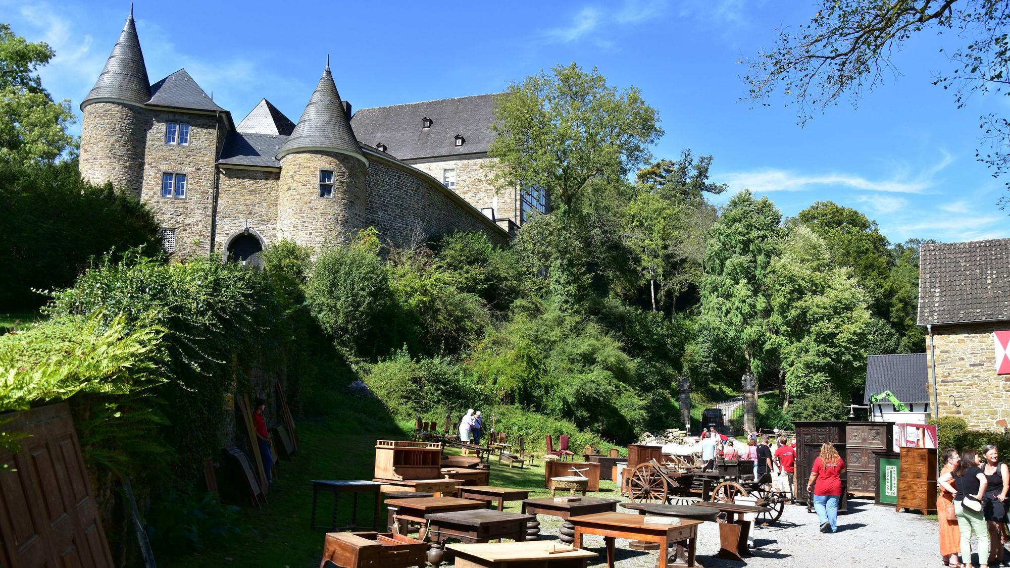 Eine alte Burg, auf einem Schotterplatz im Vordergrund stehen alte Möbel.