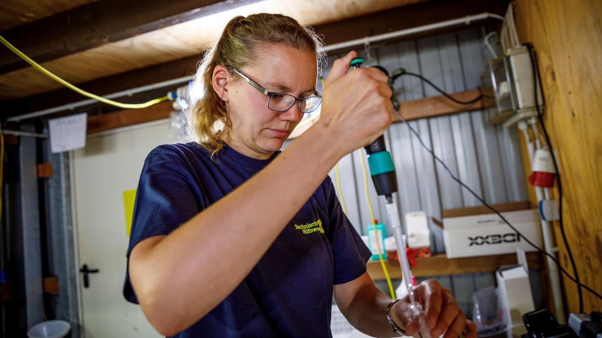 Eine Frau in einem dunkelblauen T-Shirt füllt mit einer Pipette Wasser in ein kleines Glas.