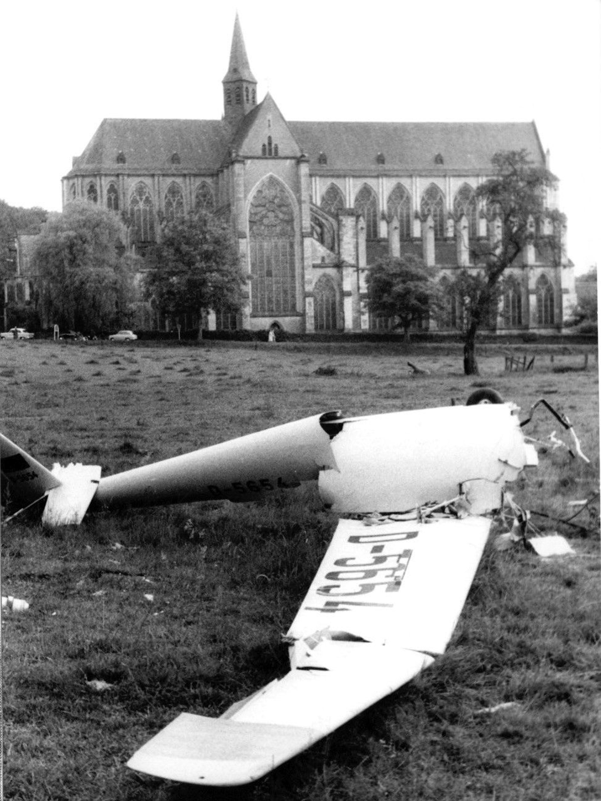 Das zerbrochene Wrack eines Segelflugzeugs liegt auf einer Wiese. Dahinter der Altenberger Dom.