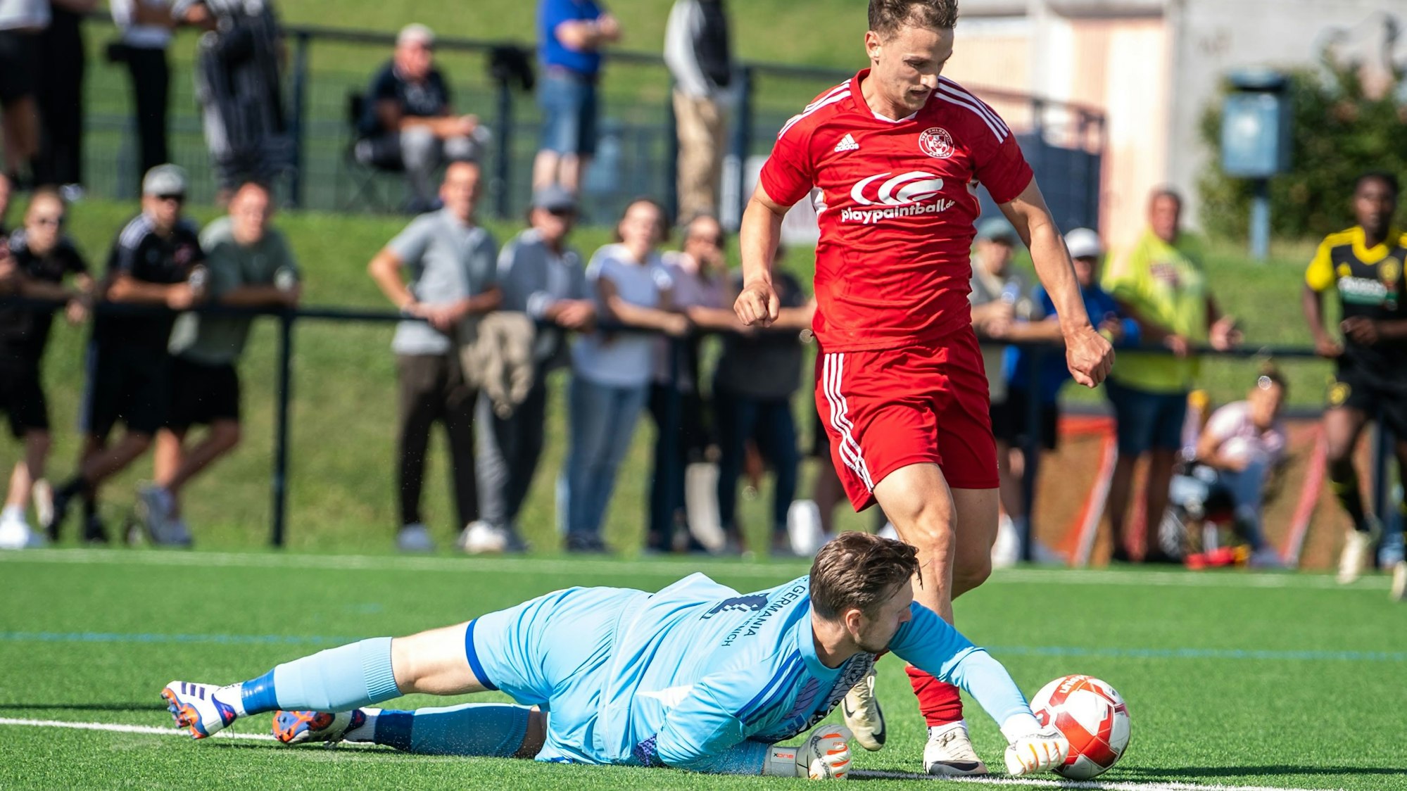 Der Torwart liegt auf dem Boden und schlägt den Ball mit der Faust weg.