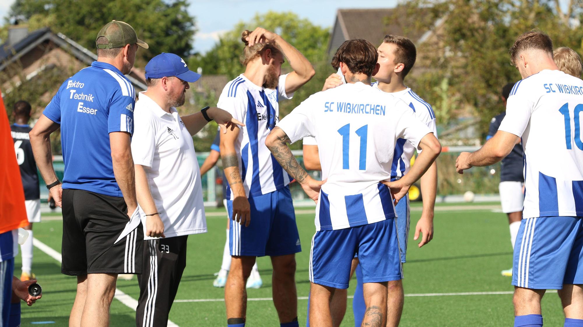 Der Co-Trainer und mehrere Spieler stehen in einer Gruppe zusammen.