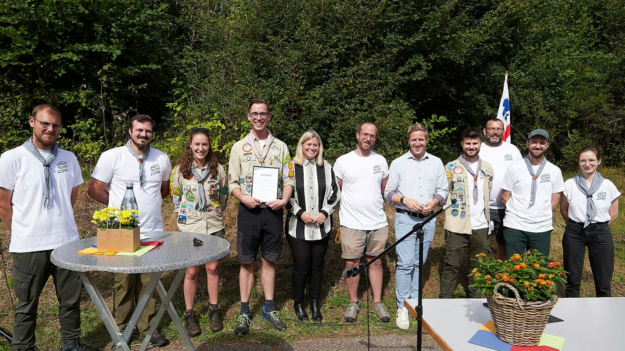Mehrere Menschen in weißen T-Shirts stehen zusammen mit Jennifer Meuren und Landrat Markus Ramers vor grünen Büschen.