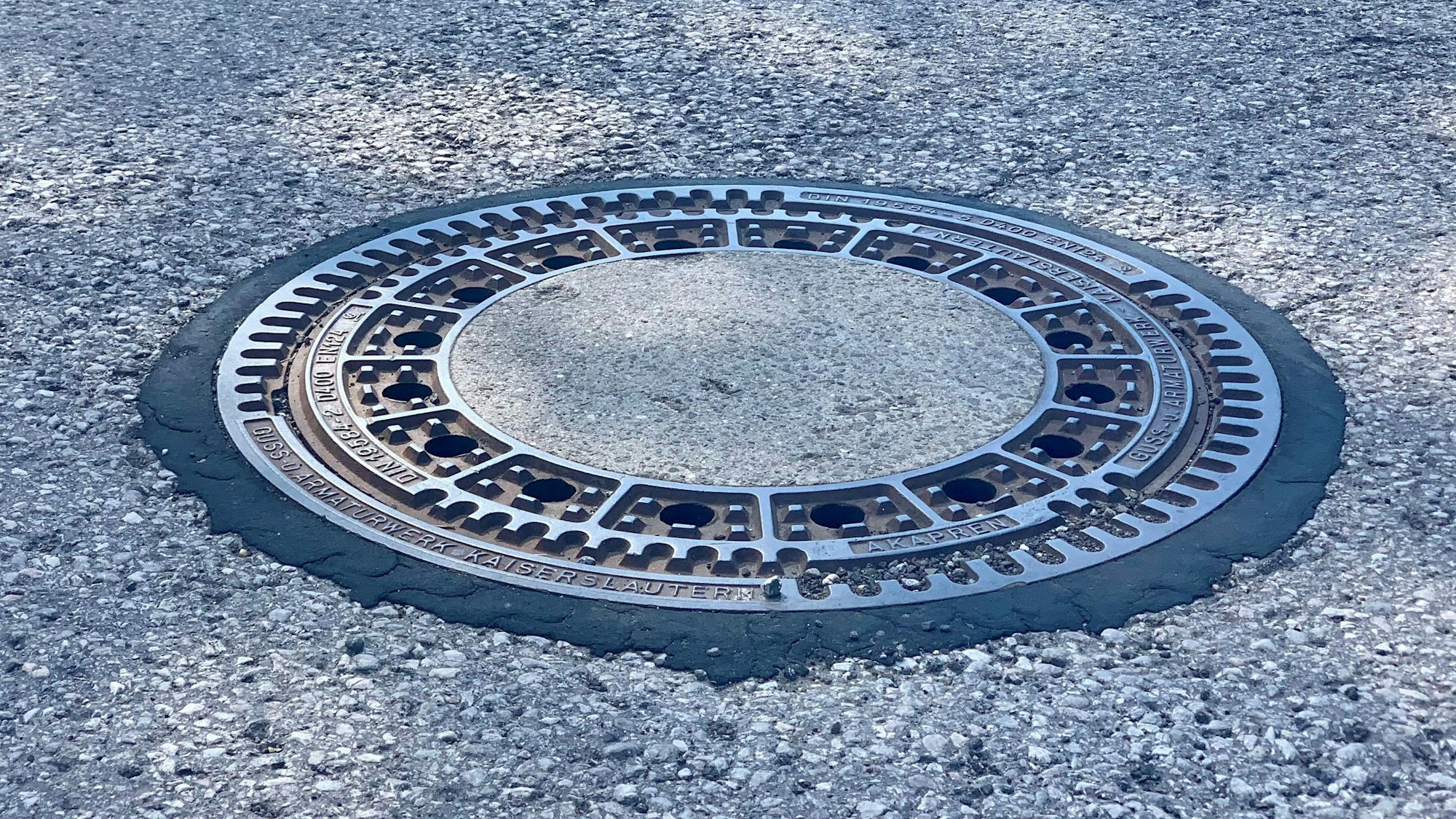 Zu sehen ist ein runder Gulli in einer Straße.