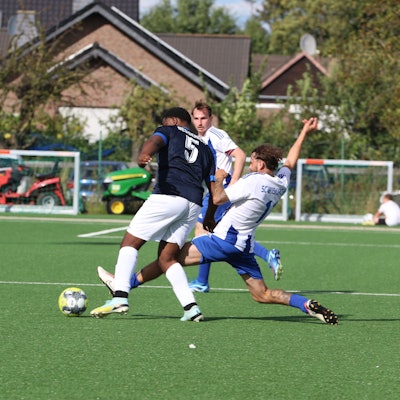 Ein Zweikampf, in dem ein Spieler mit gestrecktem Bein den Ball vor dem Gegner wegspitzelt.