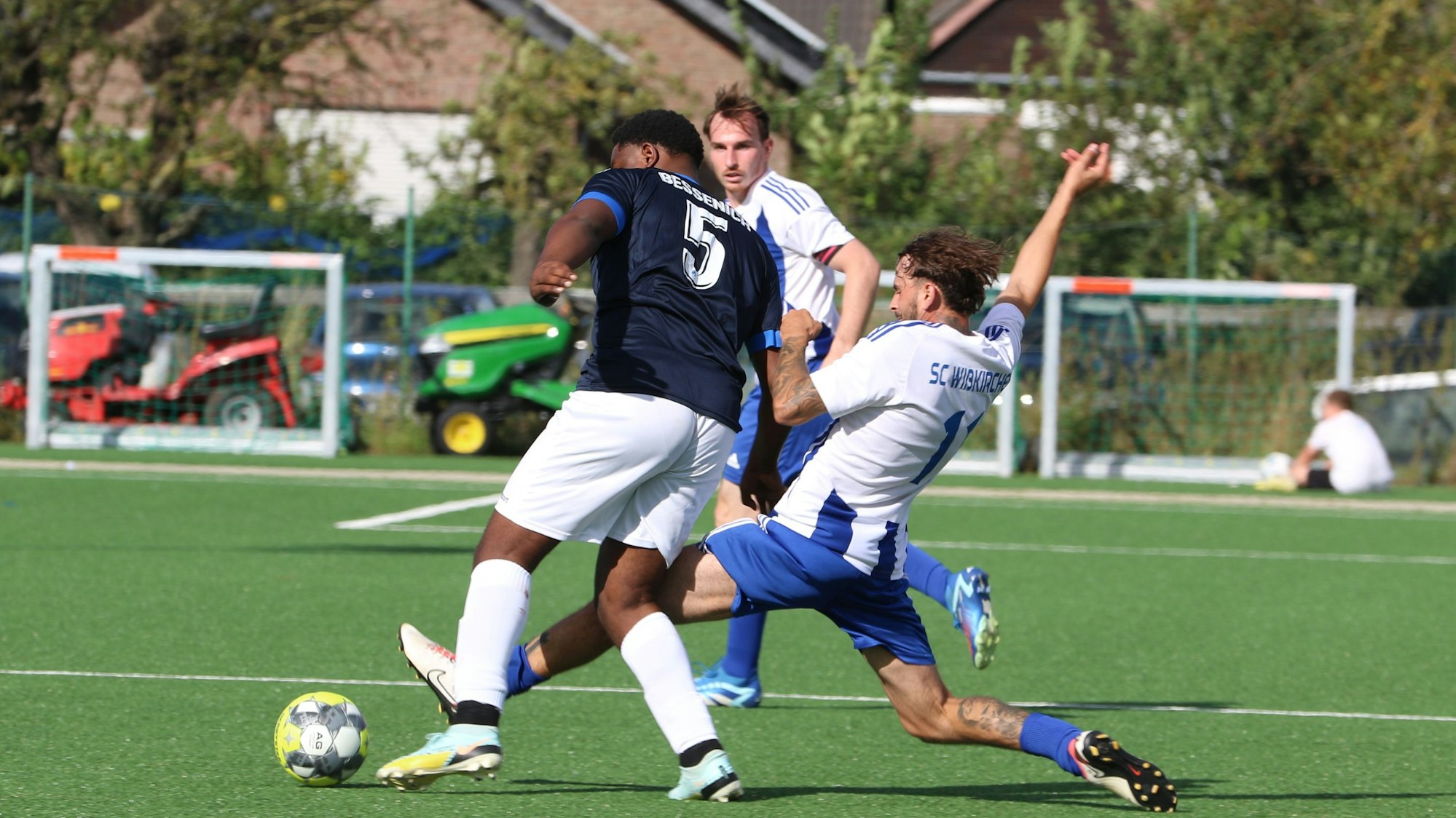 Ein Zweikampf, in dem ein Spieler mit gestrecktem Bein den Ball vor dem Gegner wegspitzelt.
