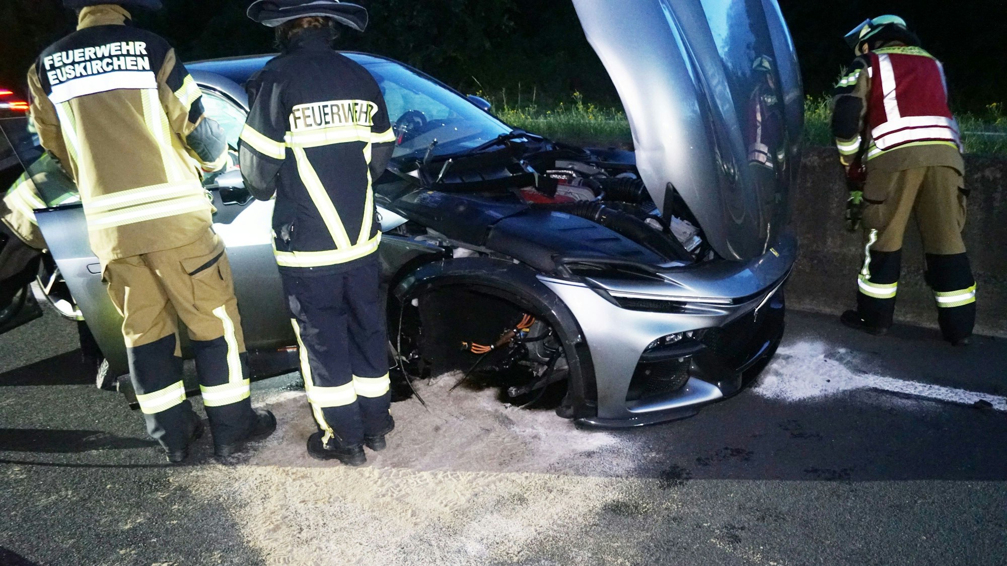 Feuerwehrleute stehen um einen zerstörten silbernen Ferrari.