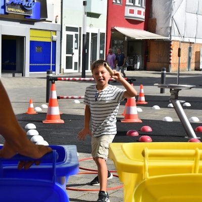 Ein Junge läuft durch einen Parcours aus kleinen Pylonen auf zwei Mülltonnen zu.