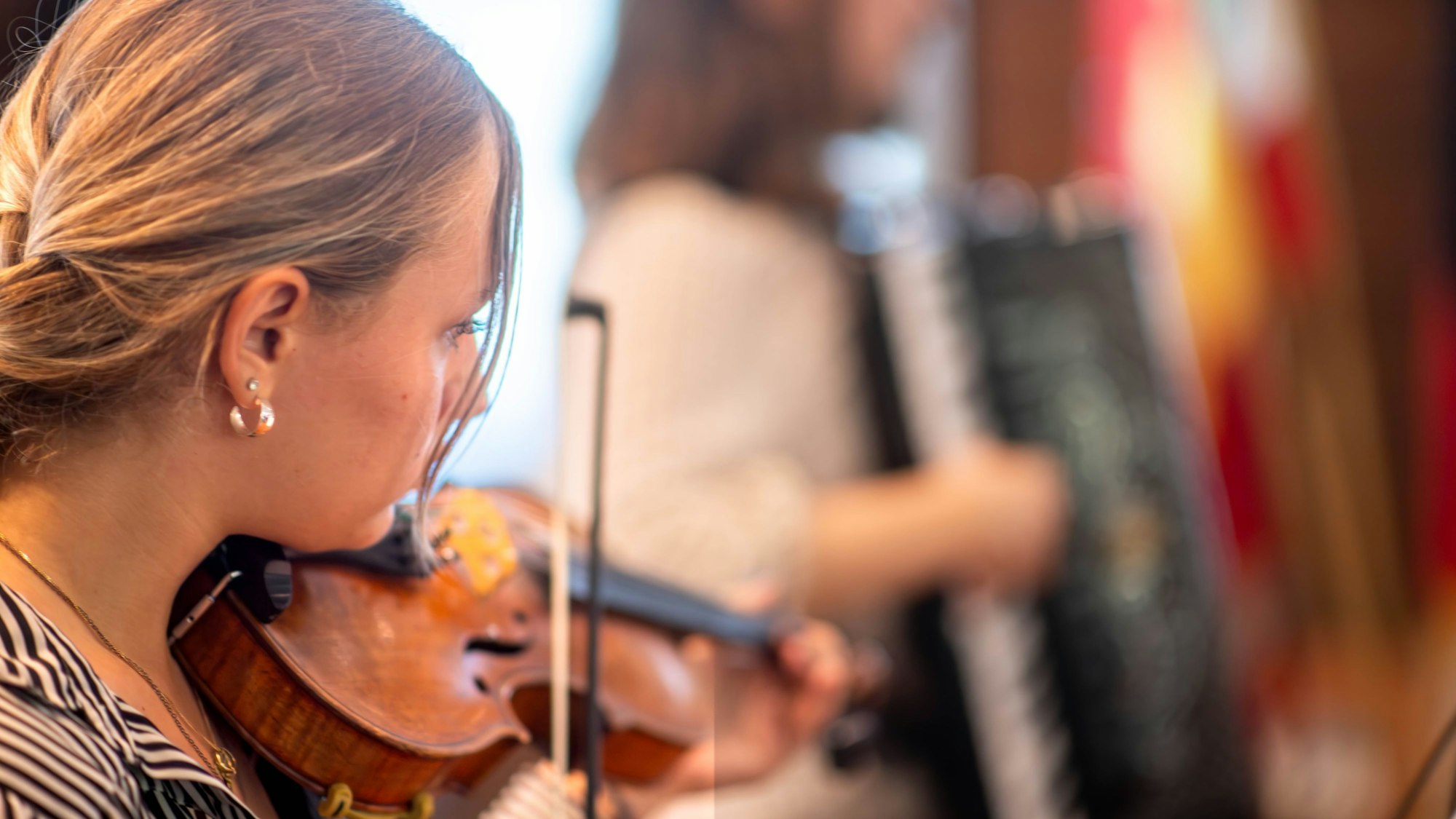 Eine blonde Frau spielt in einer schwarz-weiß gestreiften Bluse Geige.