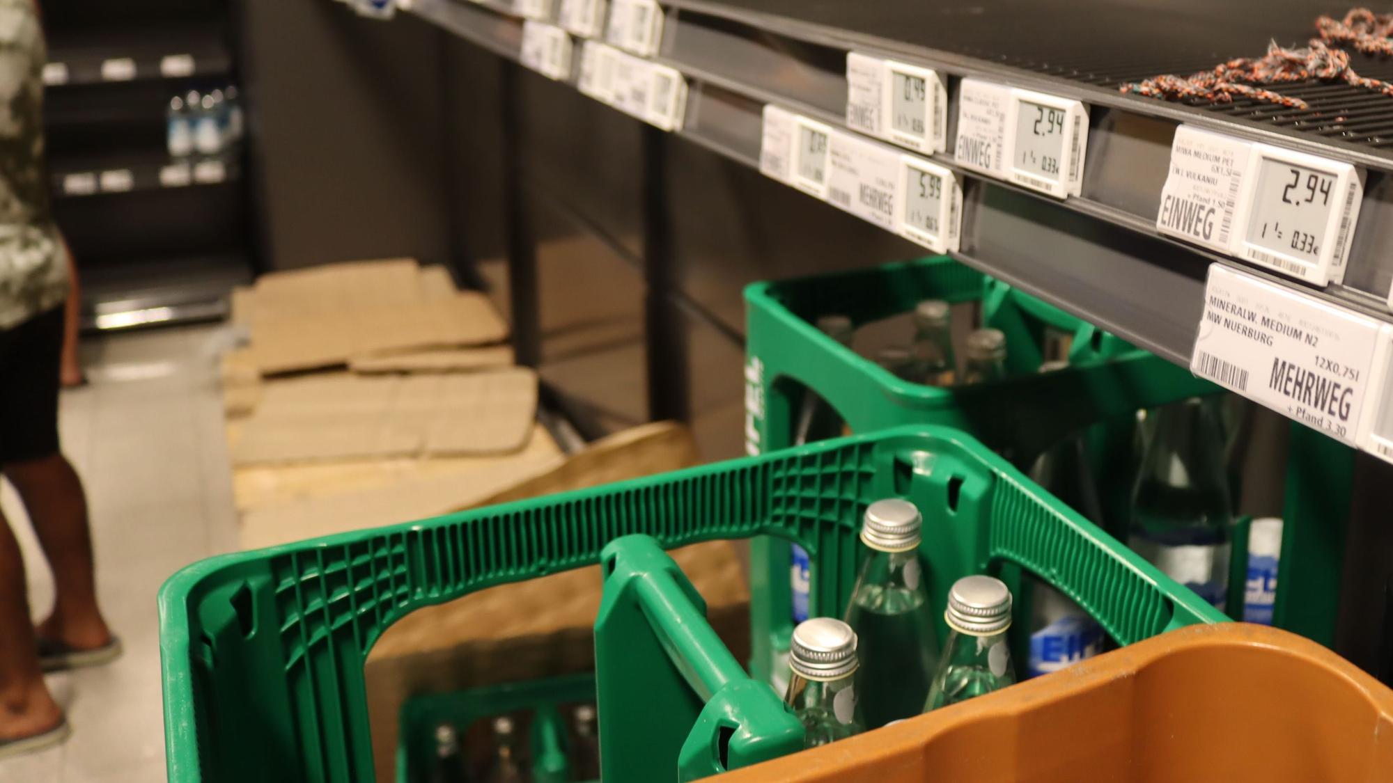Neben Wasserkästen sind leere Supermarkt-Regale zu sehen.