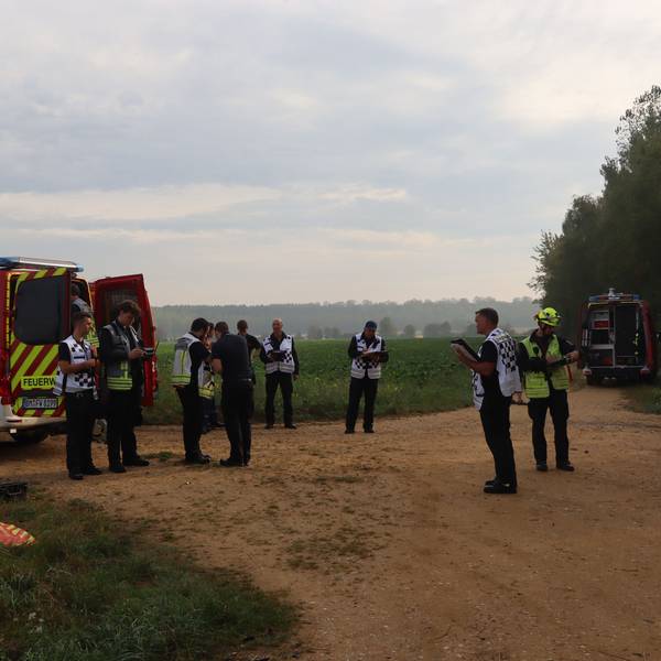 Feuerwehrleute stehen an einem Einsatzfahrzeug, am Himmel fliegt eine Drohne.