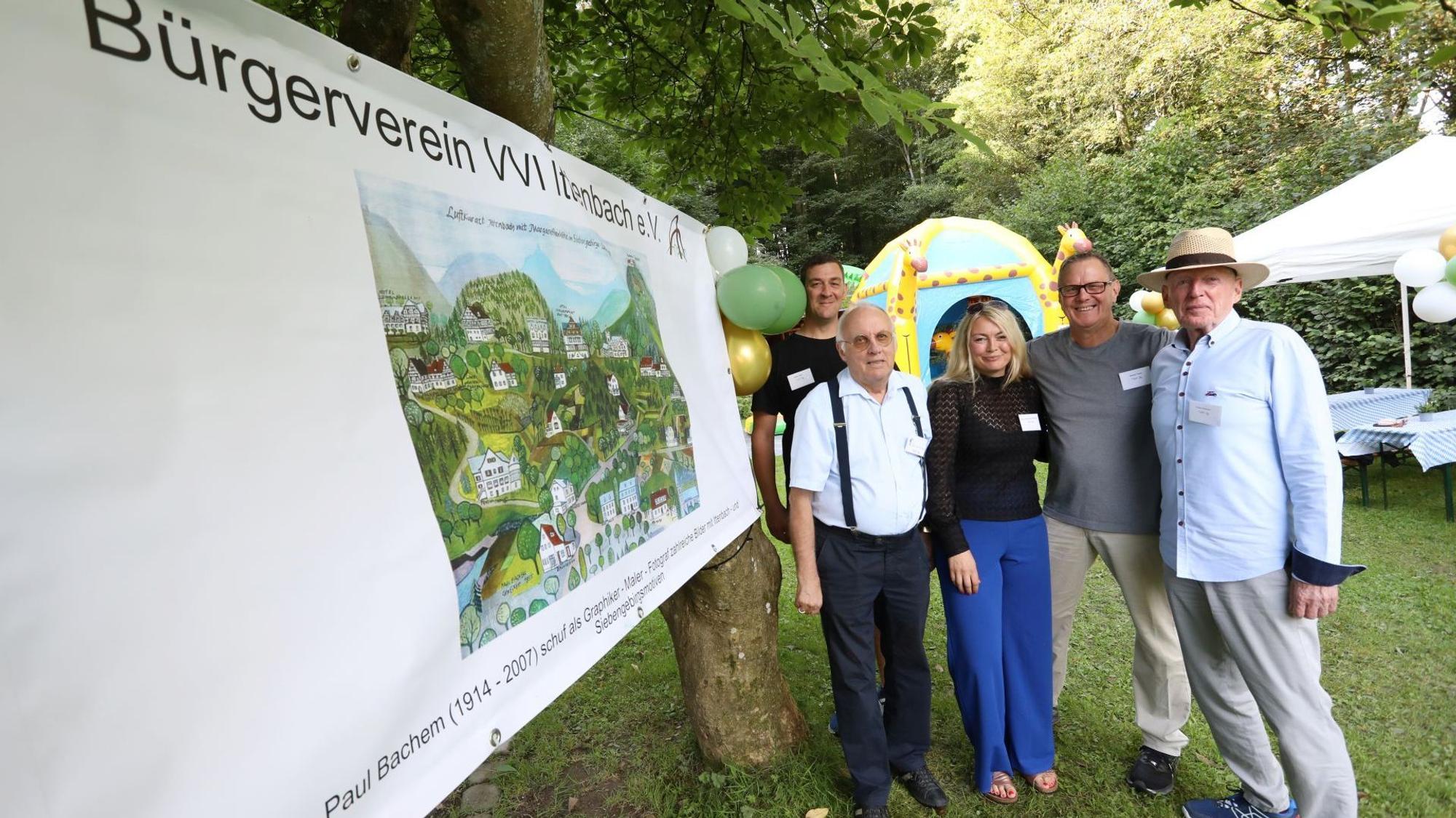 Männer und eine Frau stehen auf einer Wiese, auf der Zelte und Sonnenschirme zu sehen sind.