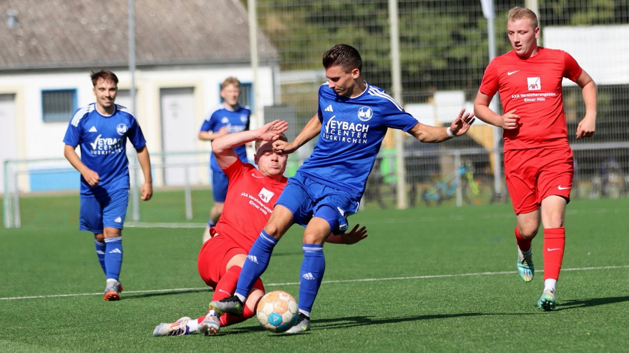 Ein Hellenthaler Spieler grätscht nach dem Ball, den ein Weilerswister Spieler am Fuß hat.