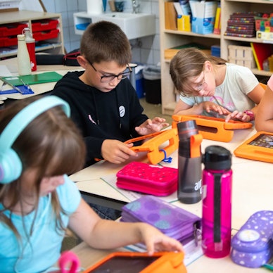 Vier Grundschülerinnen und ein Grundschüler sitzen an einem Tisch und arbeiten mit iPads.
