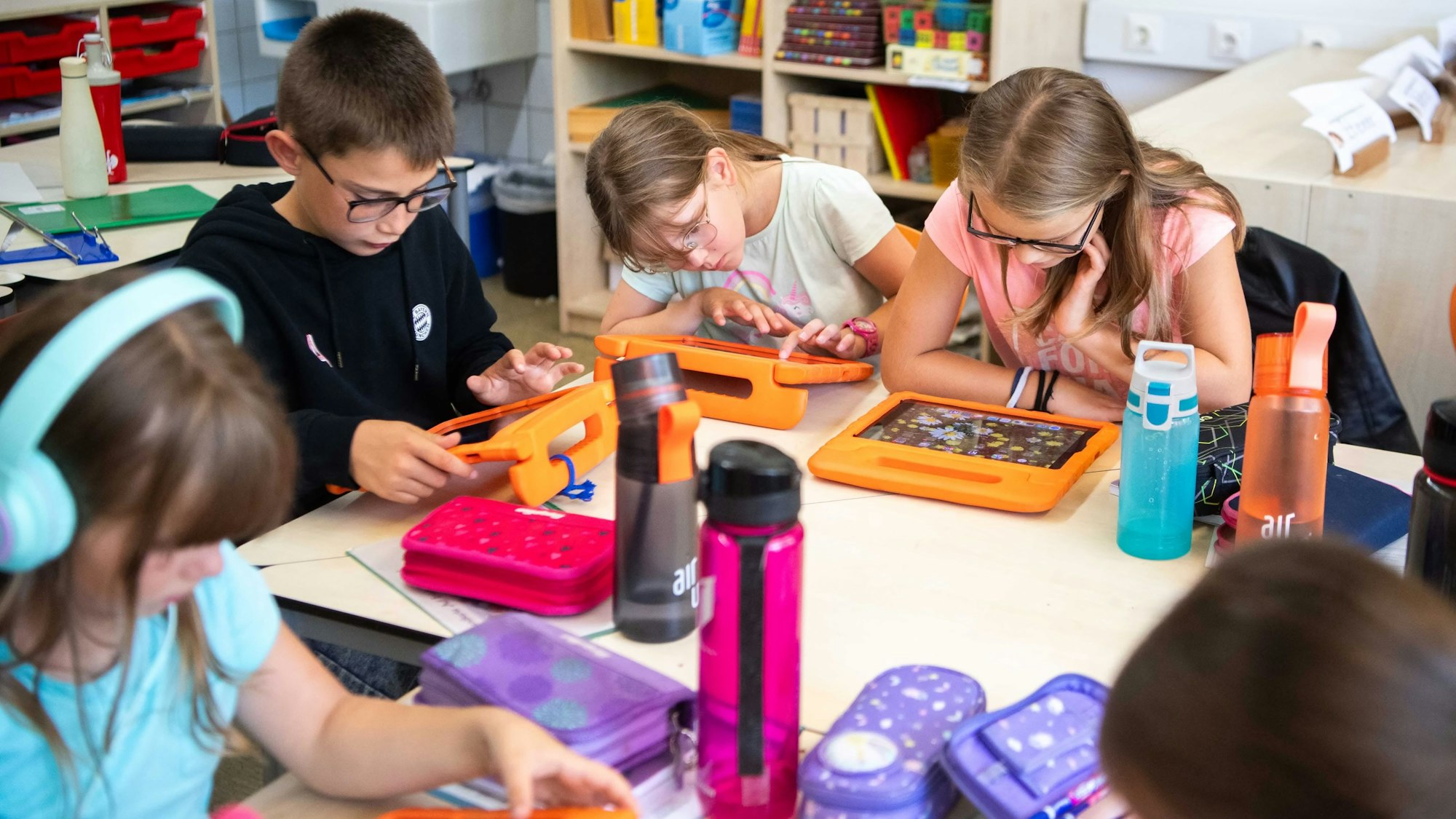 Vier Grundschülerinnen und ein Grundschüler sitzen an einem Tisch und arbeiten mit iPads.