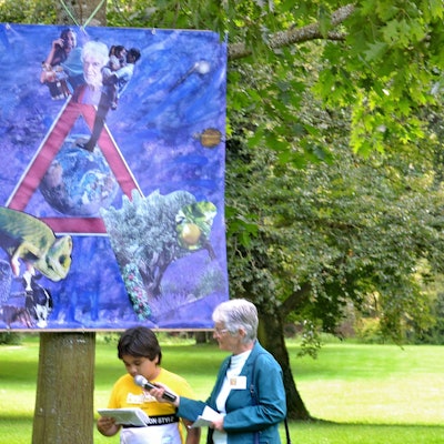 Das Bild von Solaimon hängt an einem Baum, der junge Künstler steht davor und erzählt etwas über sein Werk.