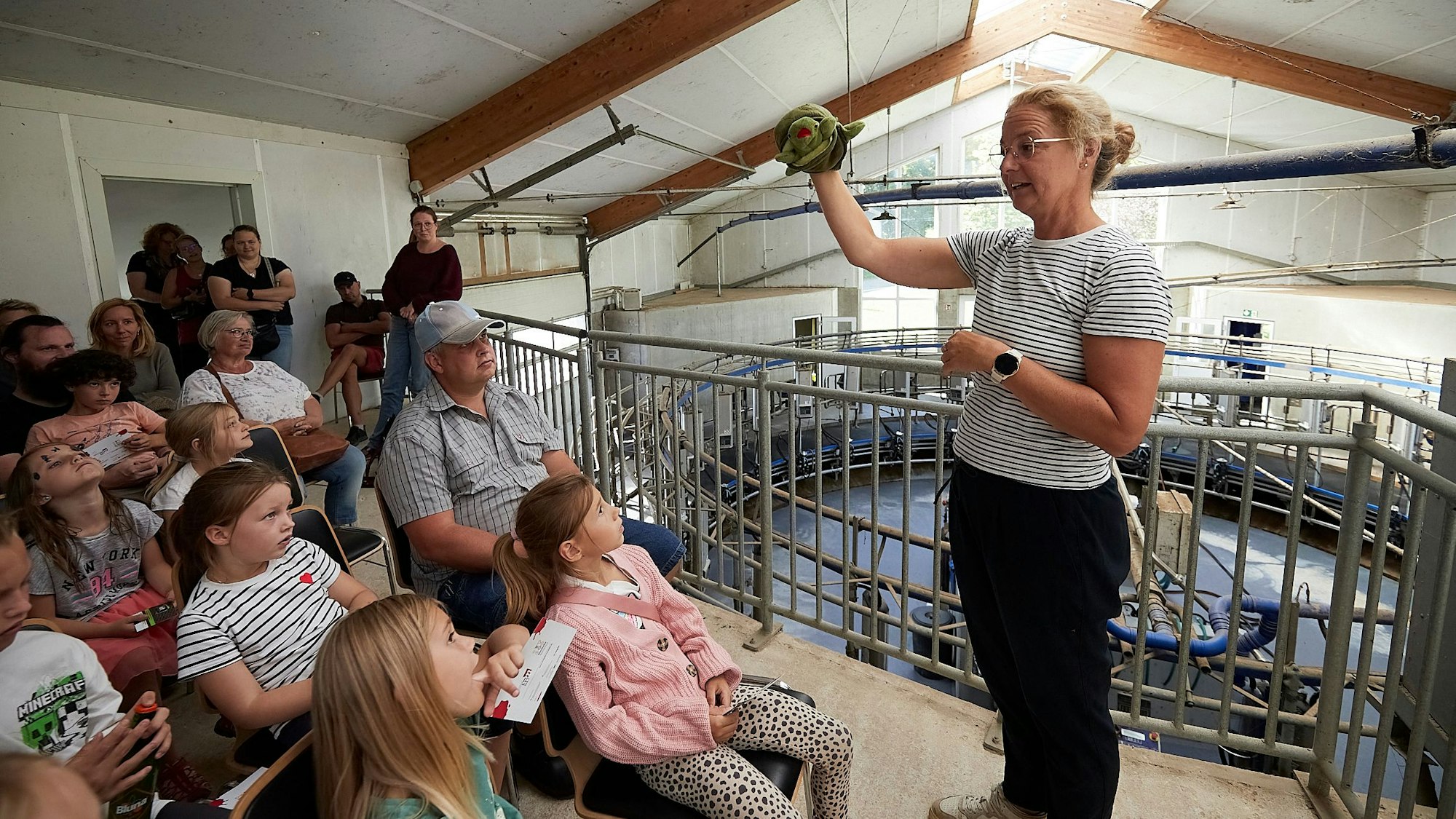 Kerstin Rottland steht vor dem Melkkarussel des Thelenshofes in Steinfelderheistert. Vor ihr sitzen die Zuhörer.