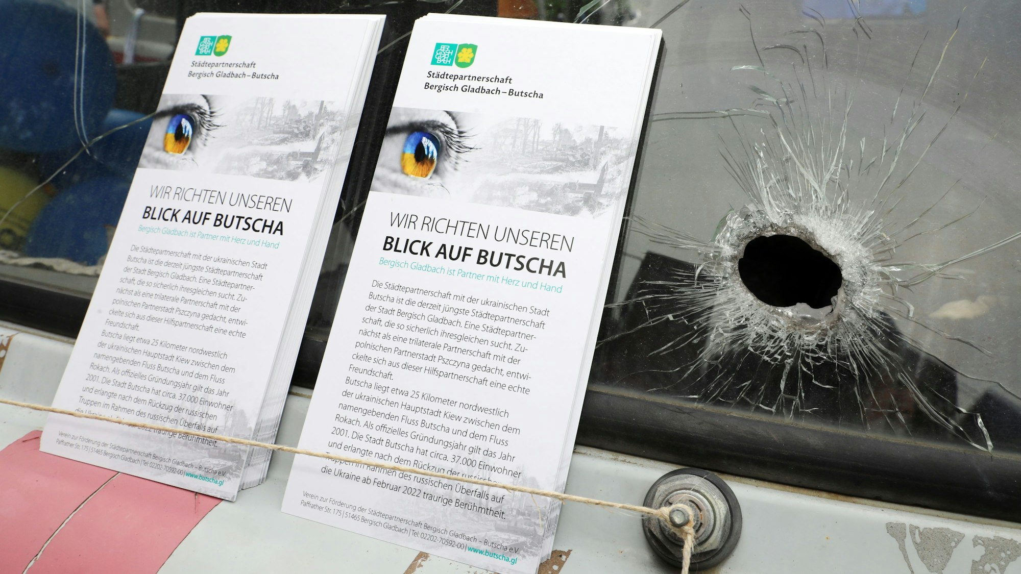 Faltblätter des Vereins zur Förderung der Städtepartnerschaft Bergisch Gladbach – Butscha stehen neben einem Loch in einer Windschutzscheibe eines ukrainischen Krankenwagens.