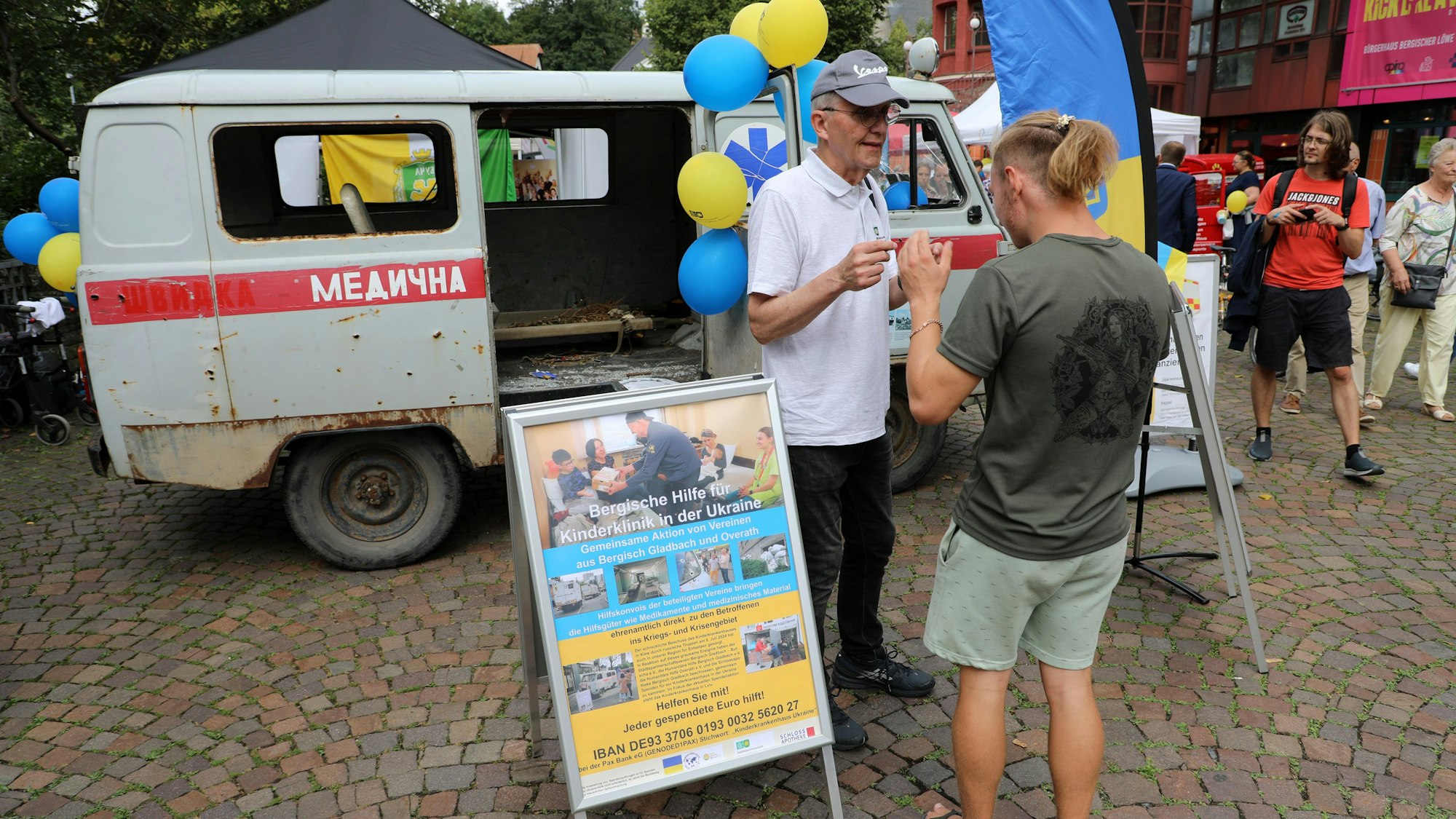 Zwei Menschen stehen vor einem zerschossenen ukrainischen Krankenwagen auf dem Stadtfest in Bergisch Gladbach.