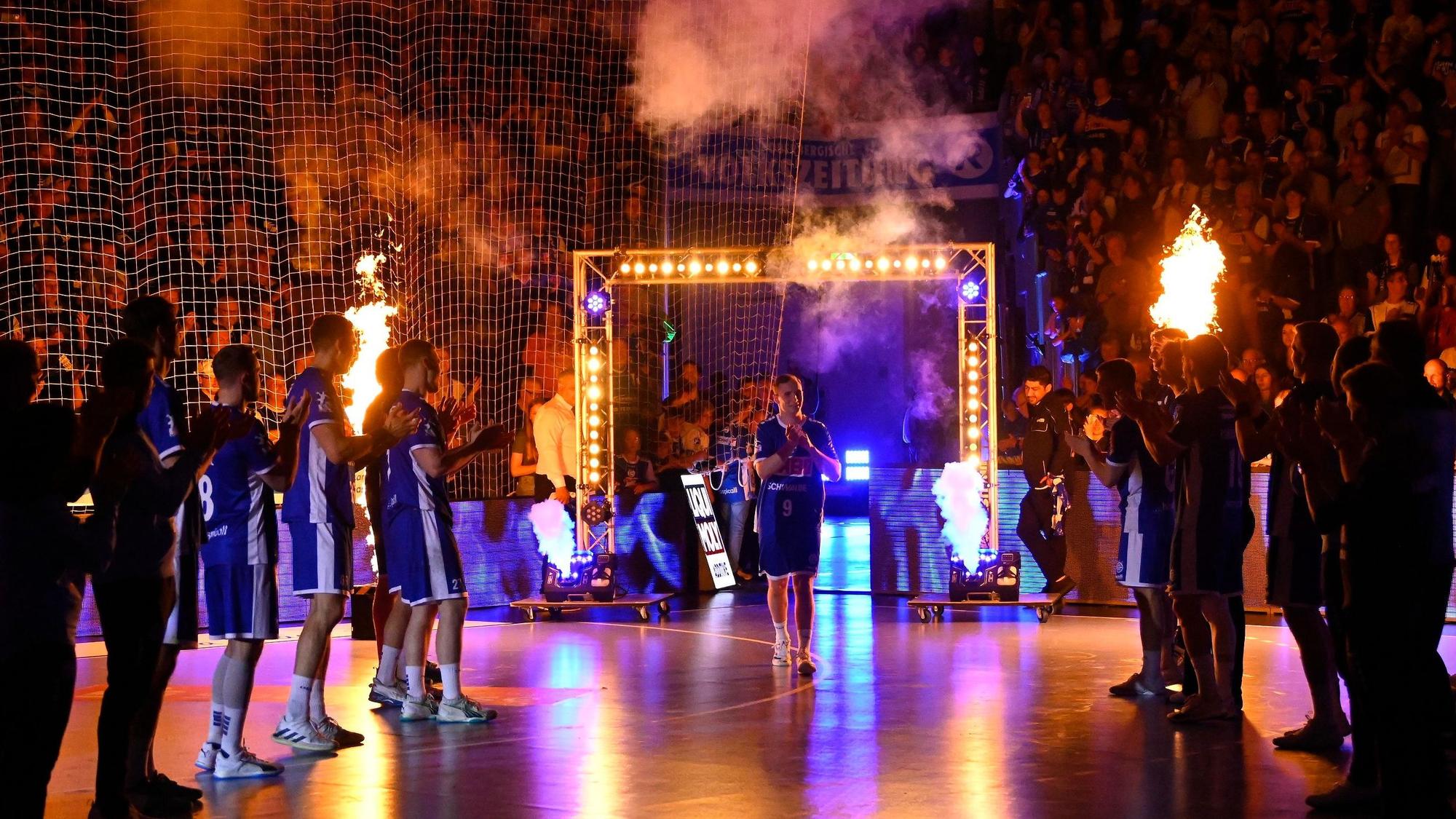 Zu sehen ist eine Szene aus der Einlaufshow einer Handball-Mannschaft mit Feuerwerk.