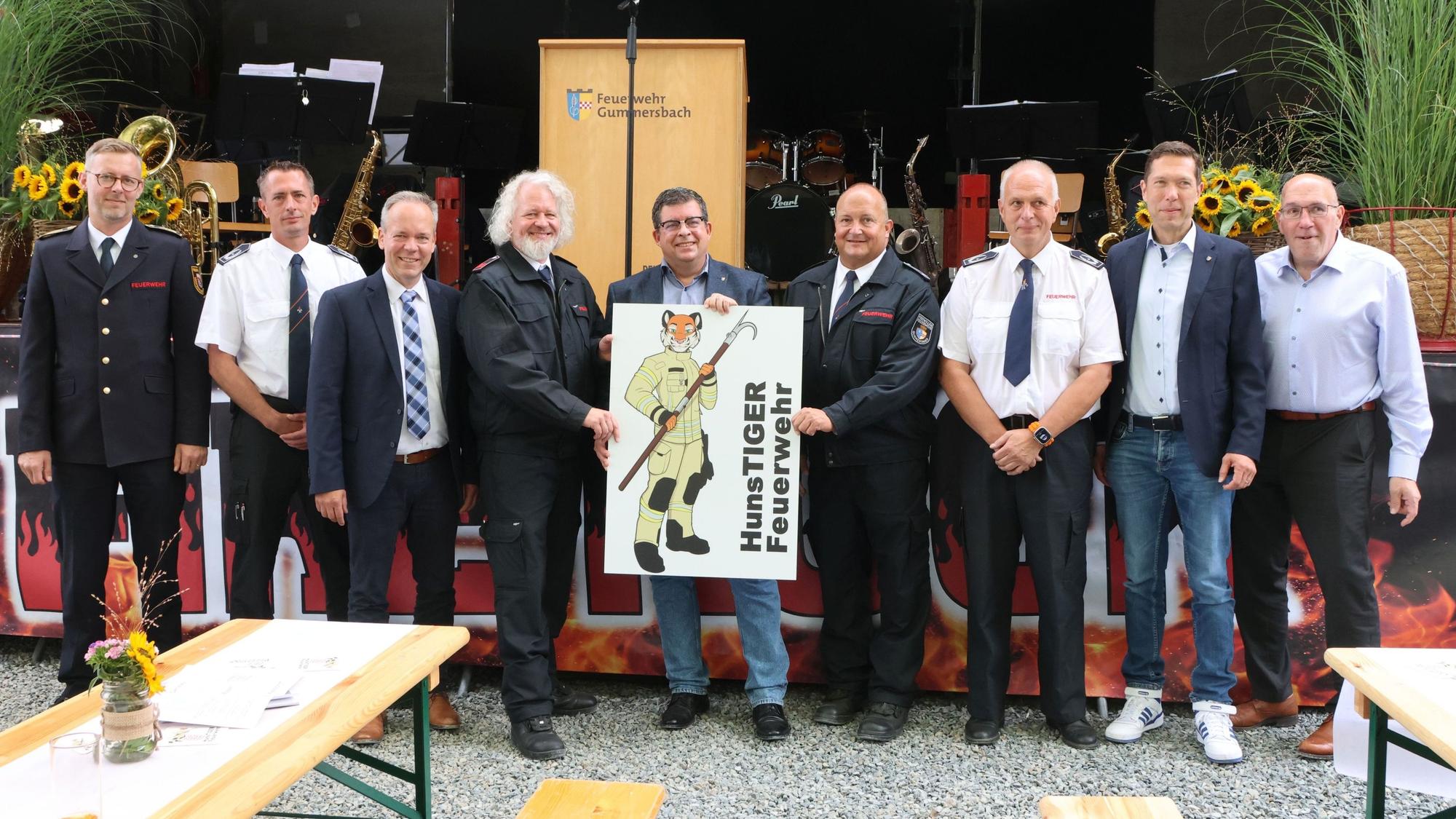 Neun Männer aus der Feuerwehr und Politik stehen mit einem Schild des Löschzugs Hunstig vor einer Bühne.