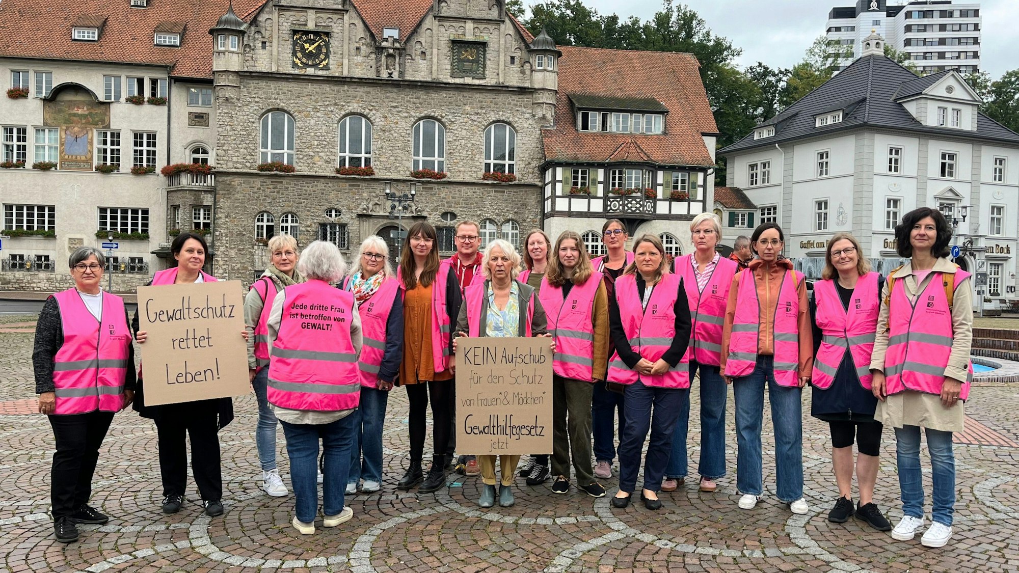 15 Teilnehmende stehen vor dem Rathaus und tragen pinke Westen.