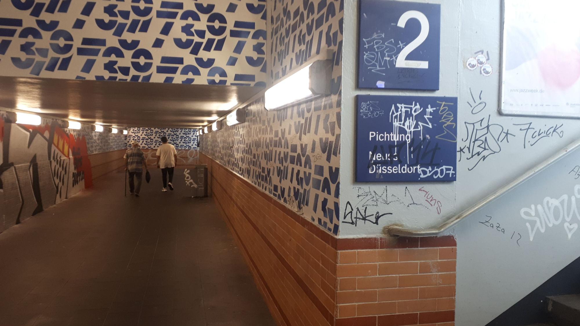 Graffiti allerorten am S-Bahnhof Longerich: Mauern, Wände, Treppenstufen, Lampen und auch Wegweiser-Schilder sind beschmiert.