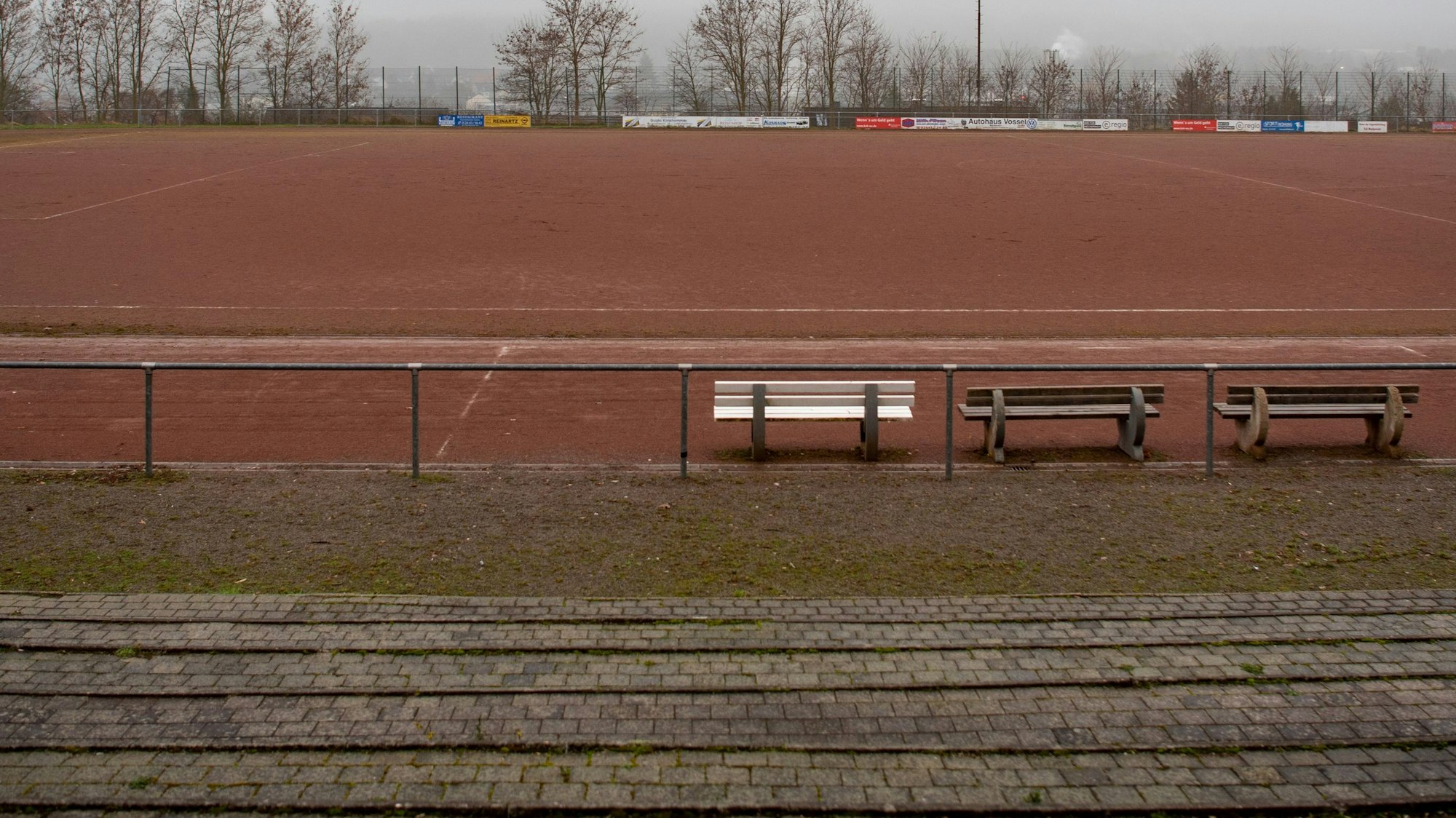 Ein Blick von der Tribüne auf das Eifelstadion. Im Vordergrund stehen drei Bänke.