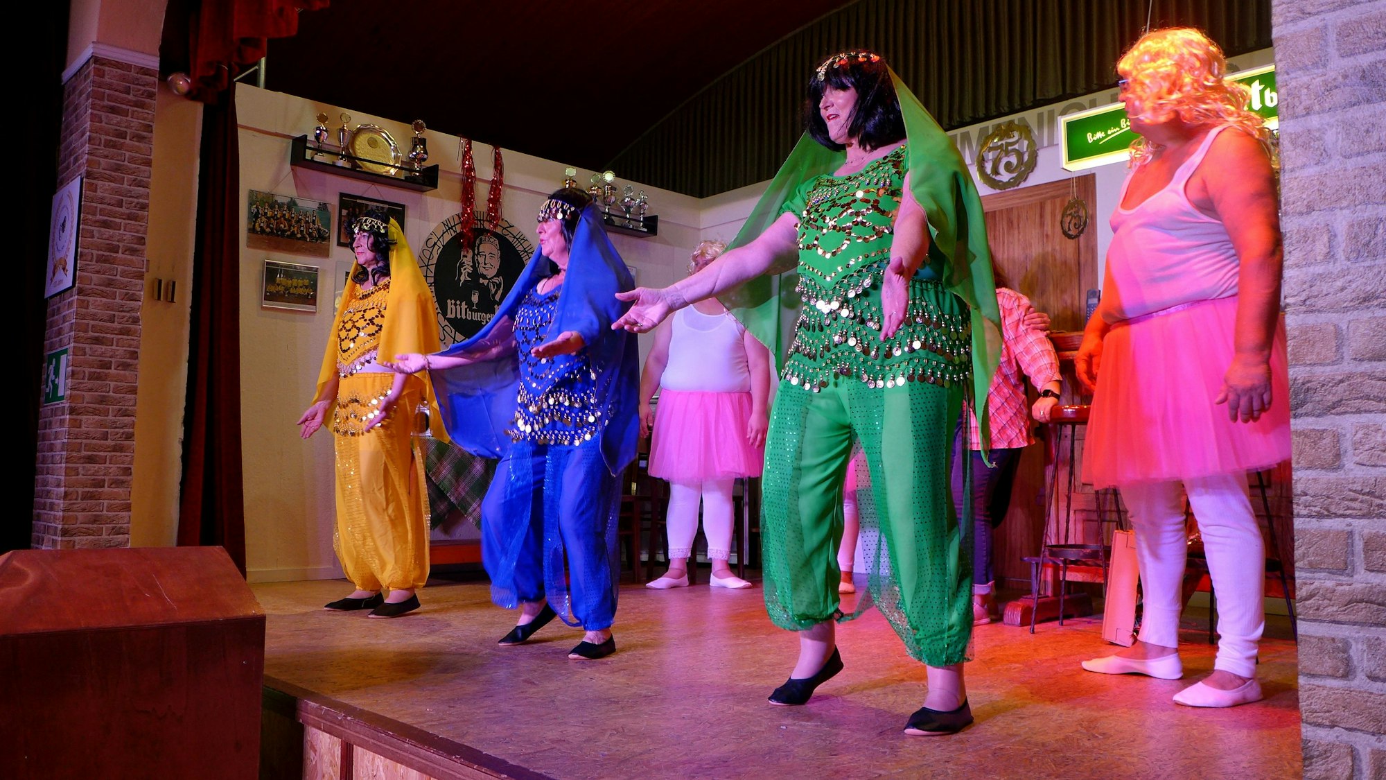 Männer und Frauen stehen in knalligen Kostümen auf einer Theaterbühne.