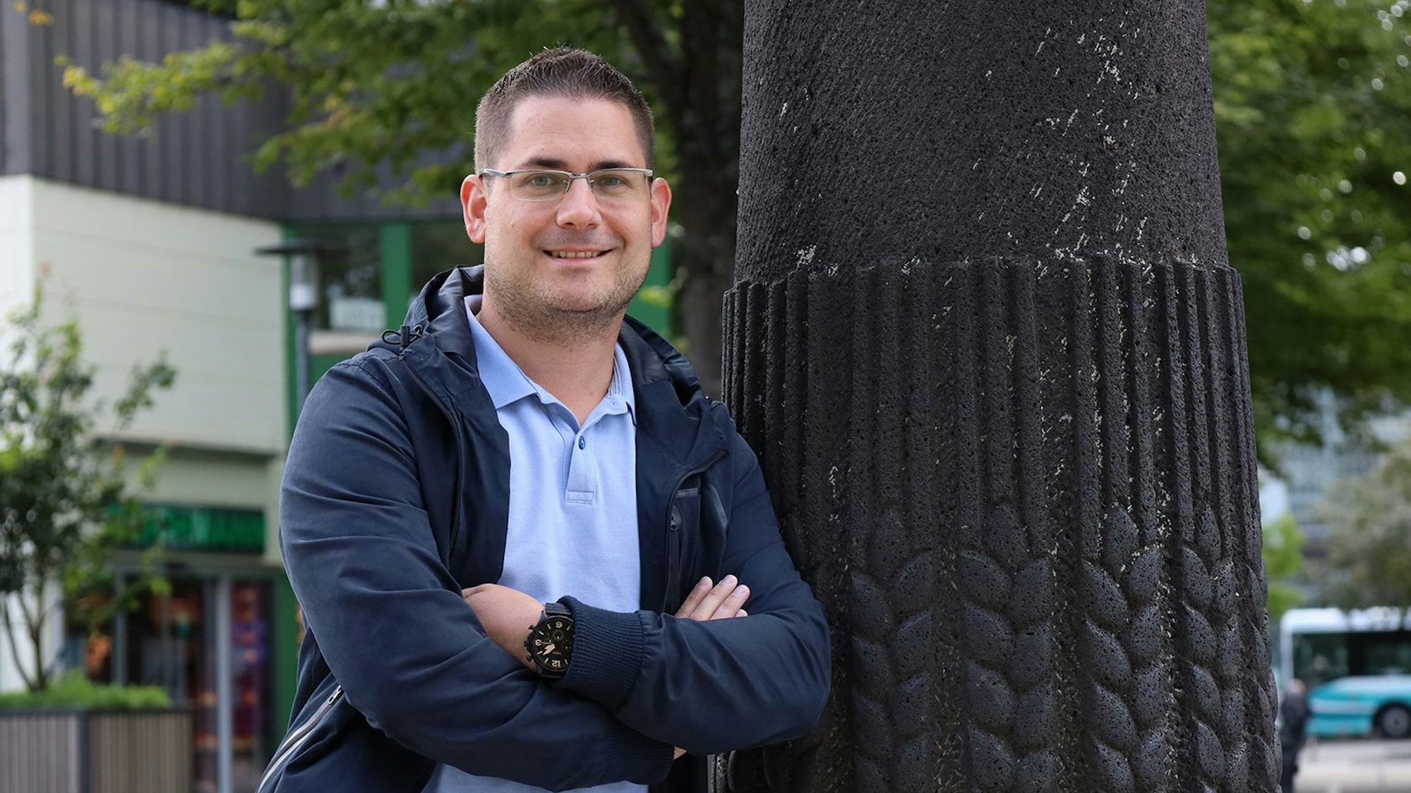 Der Mann, der den Wochenmarkt in Hennef jetzt organisiert, lehnt an eine Säule am Marktplatz.