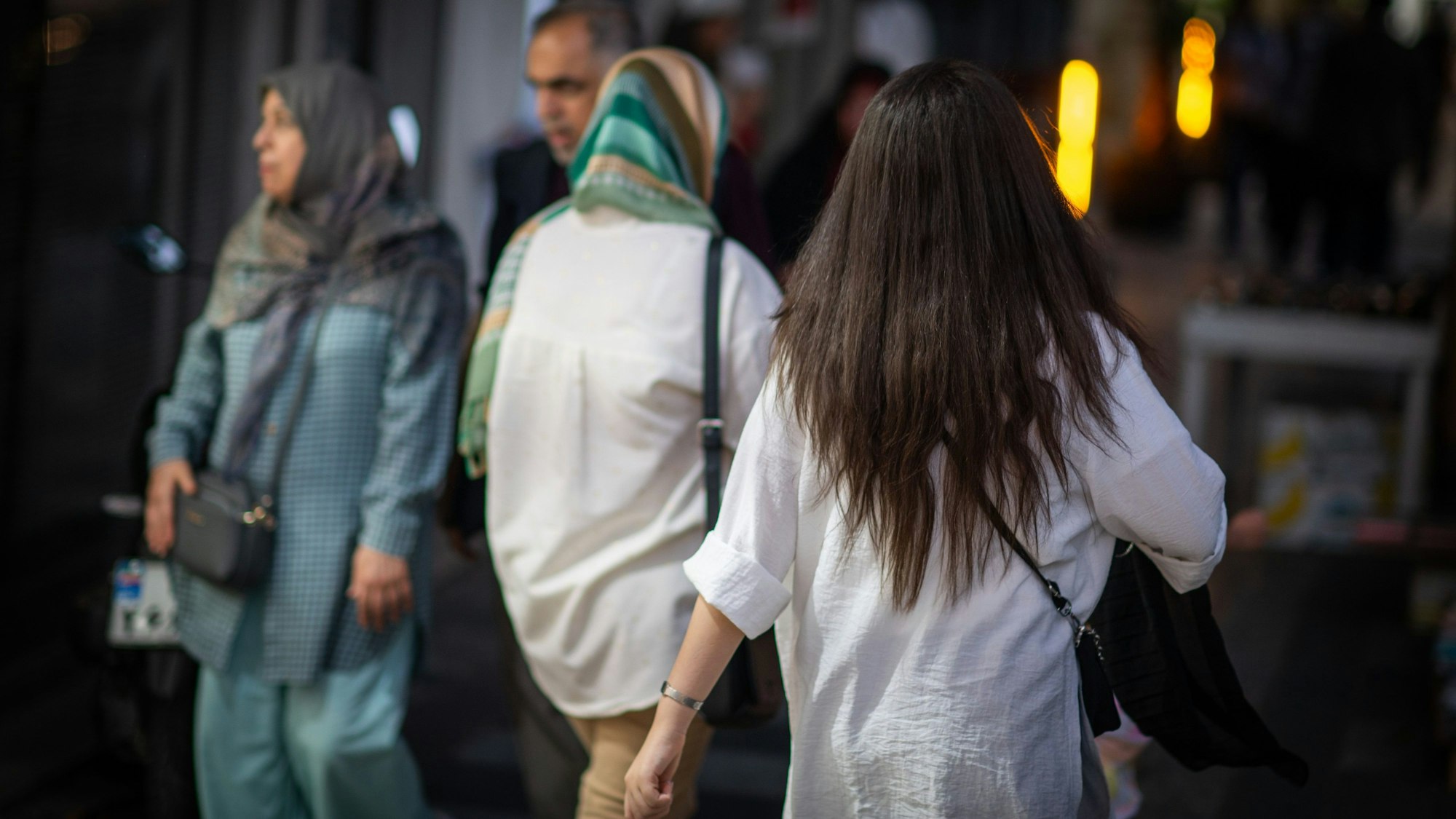 10.07.2023, Iran, Teheran: Eine Frau läuft in Teheran mit offenen Haaren am Abend eine Straße entlang.