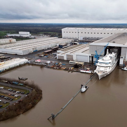 Ein Bild des Geländes der Meyer Werft von oben. Ein Kreuzfahrtschiff verlässt das überdachte Baudock der Meyer Werft.