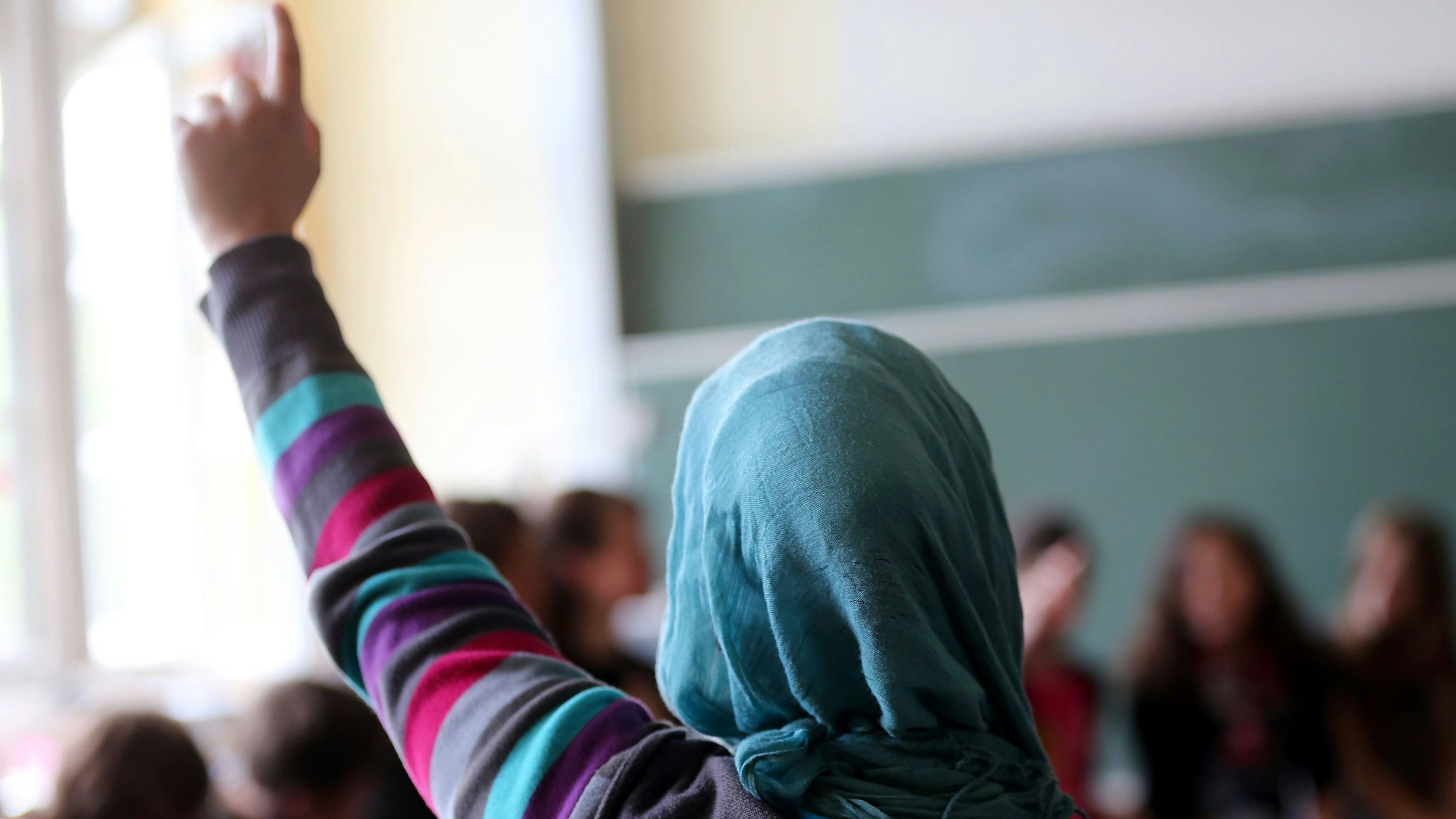 Eine Schülerin mit Kopftuch meldet sich im Unterricht.