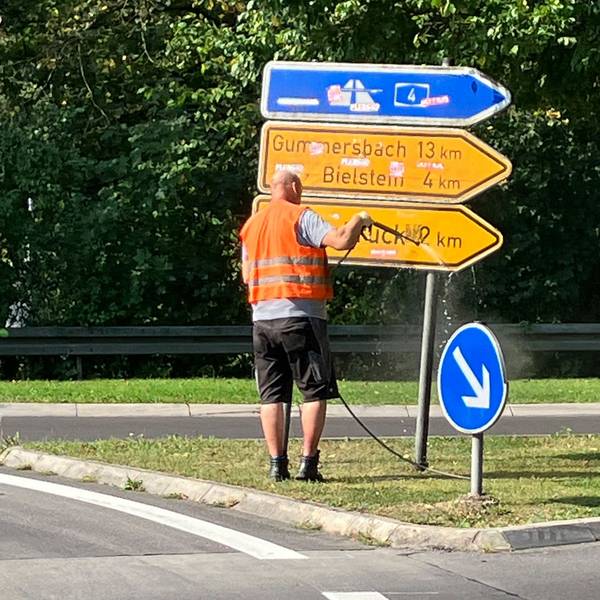 Ein Mann in Warnweste spritzt ein Hinweisschild ab.