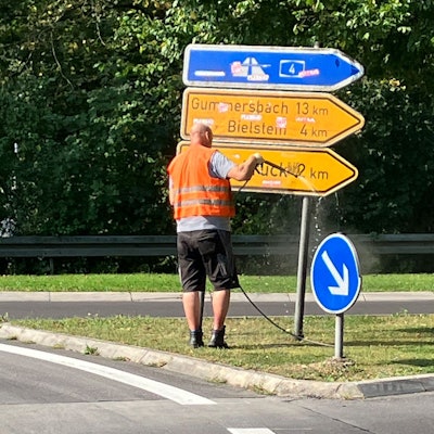 Ein Mann in Warnweste spritzt ein Hinweisschild ab.