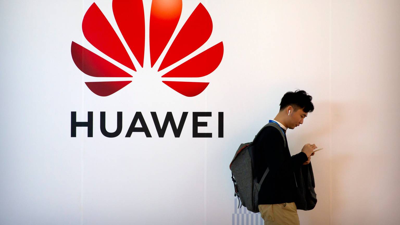 Ein Mann tippt auf seinem Smartphone, während er in der Nähe einer Werbetafel für die chinesische Technologiefirma Huawei steht.