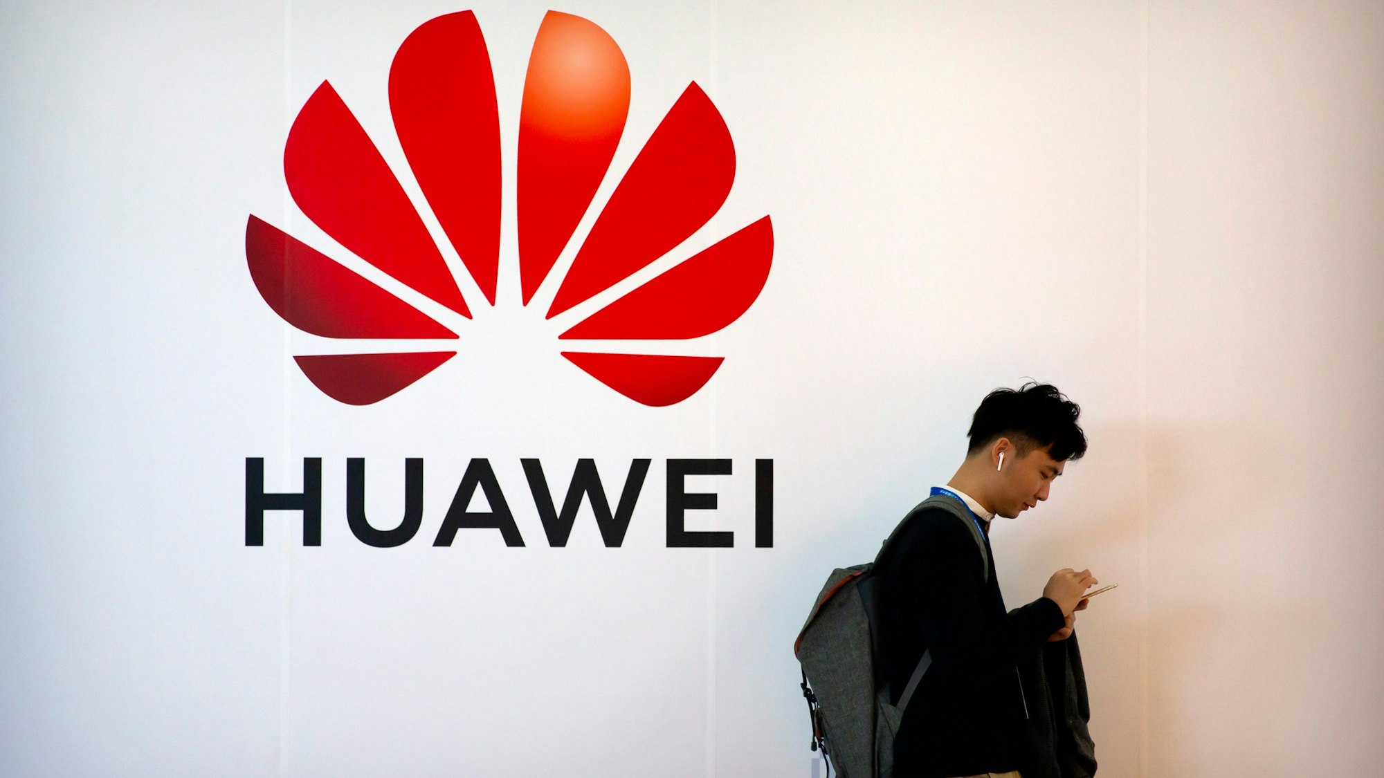 Ein Mann tippt auf seinem Smartphone, während er in der Nähe einer Werbetafel für die chinesische Technologiefirma Huawei steht.