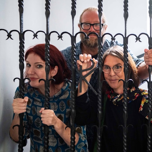 Das Bild zeigt die drei Autoren, die sich für ein gestelltes Foto hinter die Gittertür in der Kirche der JVA gestellt haben.