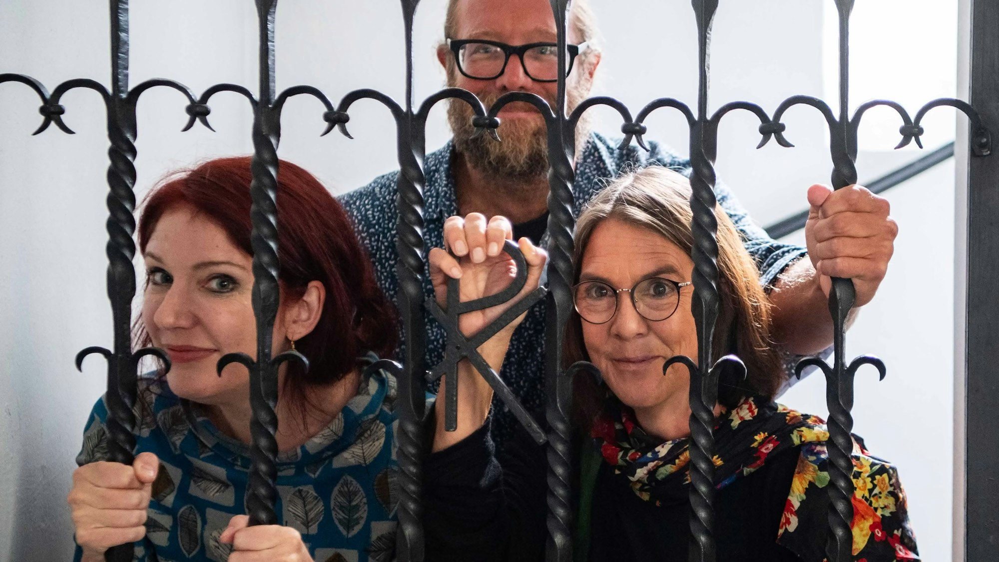 Das Bild zeigt die drei Autoren, die sich für ein gestelltes Foto hinter die Gittertür in der Kirche der JVA gestellt haben.