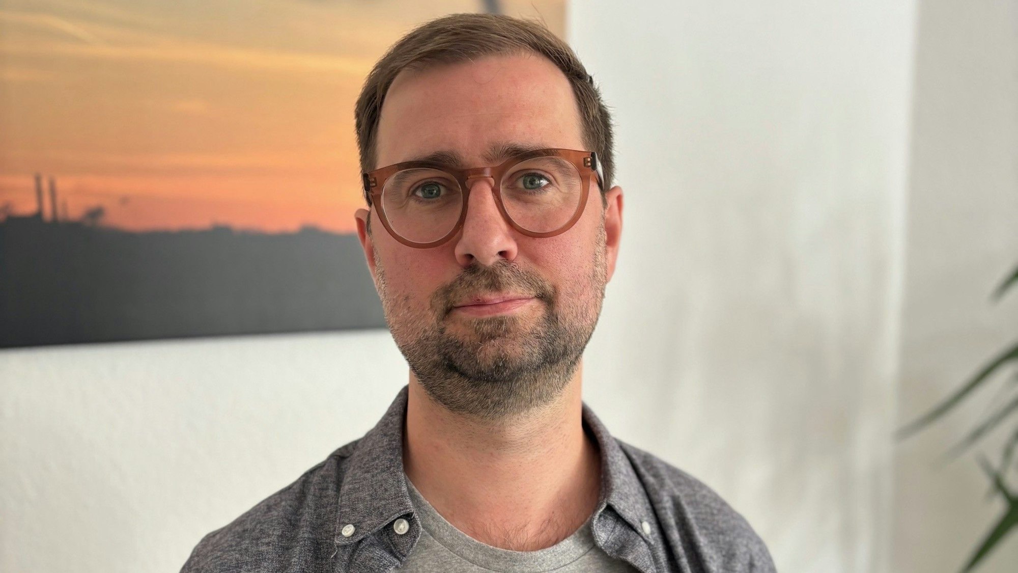 Auf dem Bild ist ein Portrait von Dominik Schmitz zu sehen, er träft ein graues Shirt und ein graues Hemd.