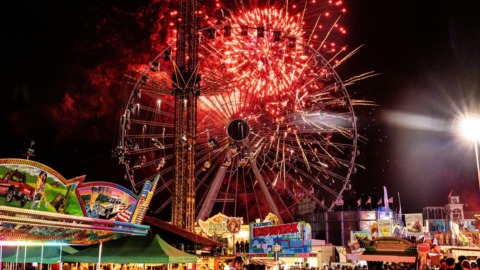 Hinter einem Riesenrad erleuchtet Feuerwerk den Nachthimmel.