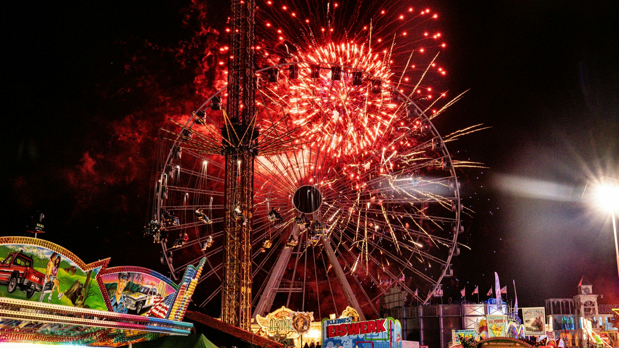 Hinter einem Riesenrad erleuchtet Feuerwerk den Nachthimmel.
