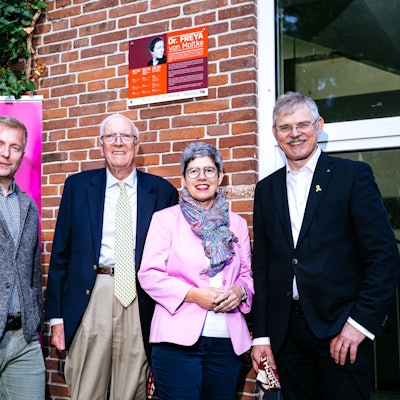 Vier Menschen stehen vor eine Tafel mit Foto und Lebensdaten von Freya von Moltke.