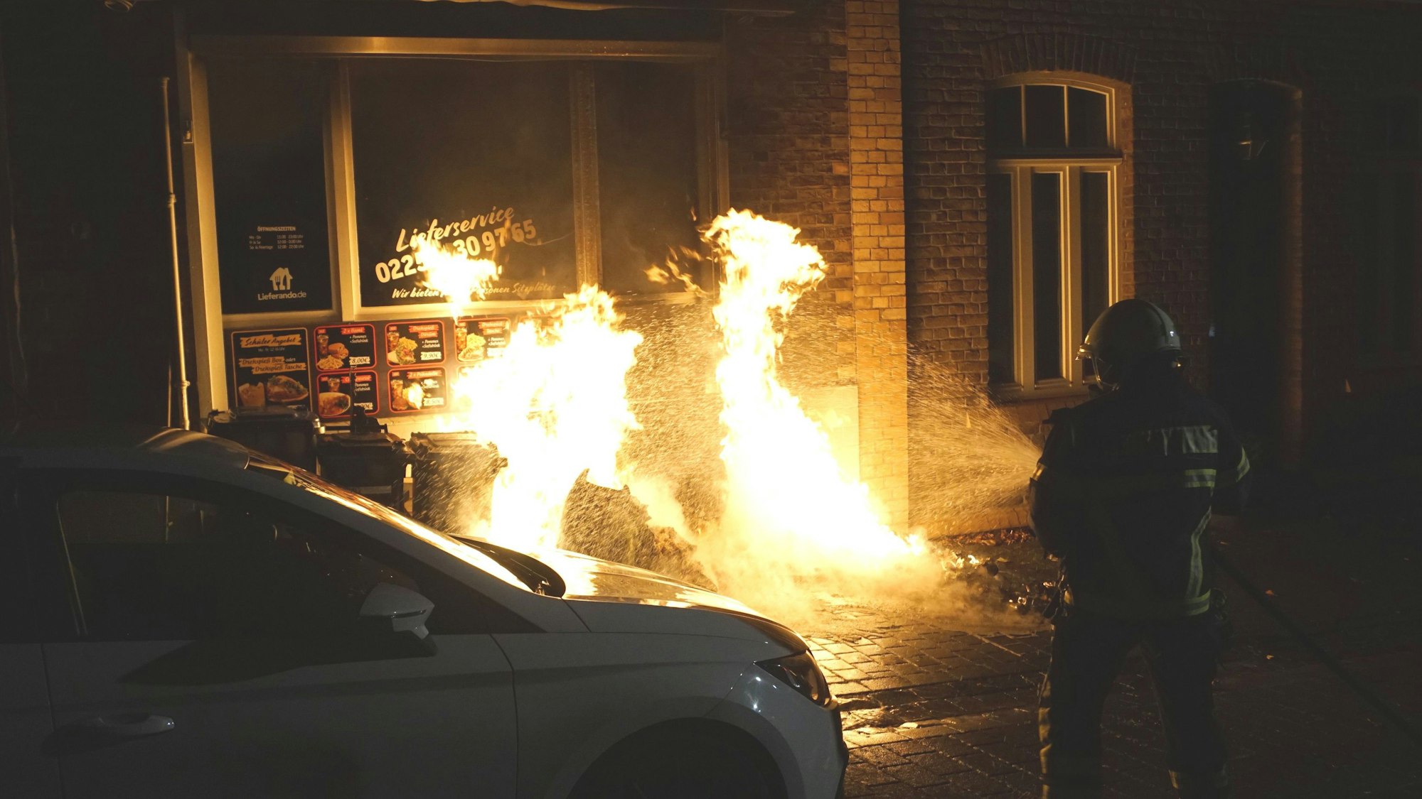 Das Bild zeigt einen Feuerwehrmann, der Flammen vor einem Schaufenster löscht.