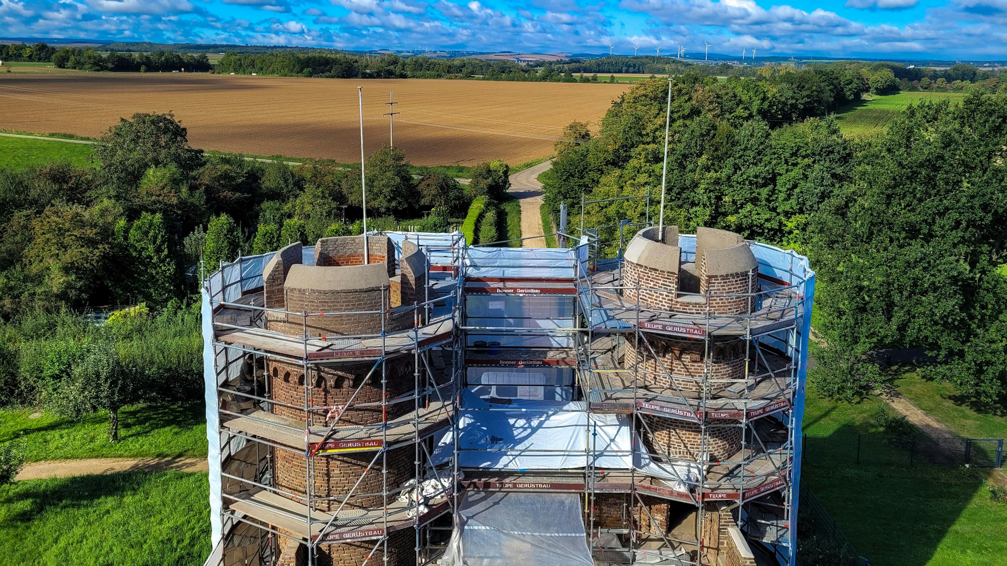 Blick vom Dach des Weiertors in Richtung Vettweiß: Vorne sieht man die noch eingerüsteten kleineren Türme des Tors, dahinter Felder und Bäume und am Horizont Windräder.