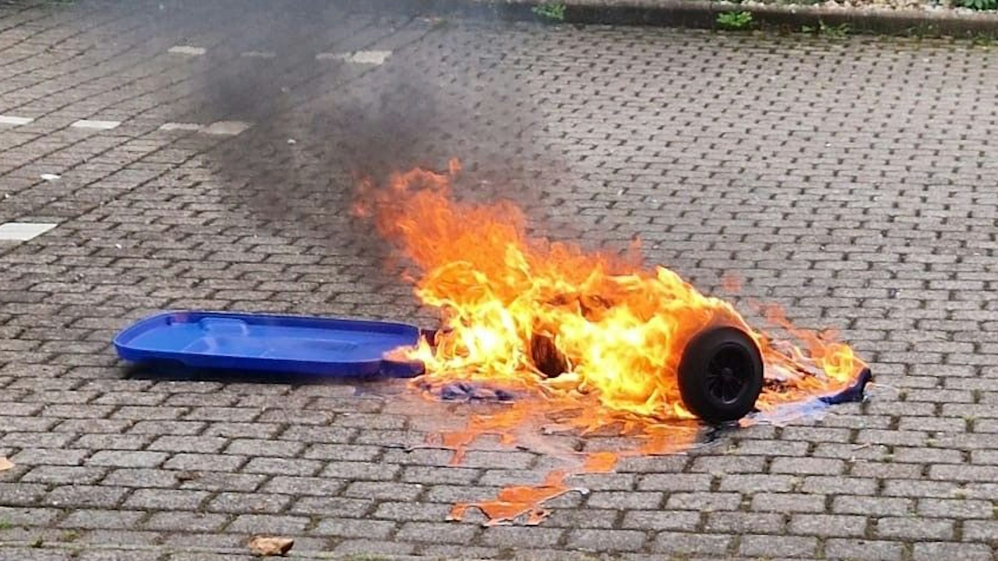 Eine brennende Mülltonne liegt auf einem gepflasterten Platz.